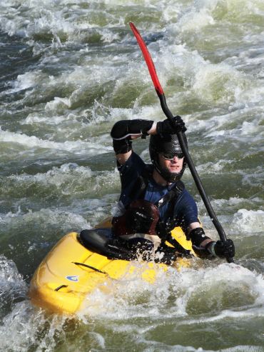 A kayaker paddling through rough whitewater rapids in a yellow kayak.