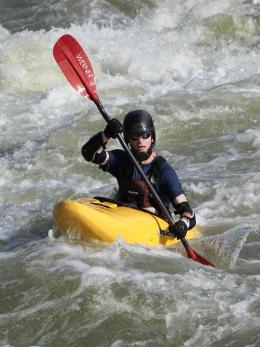 A kayaker navigates whitewater rapids in a yellow kayak.
