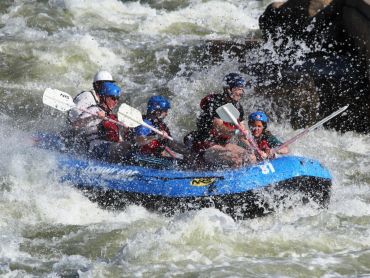 Group rafting through white-water rapids with paddles in hand.