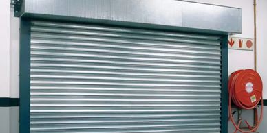 Metal rolling shutter door with fire hose reel nearby in a building.