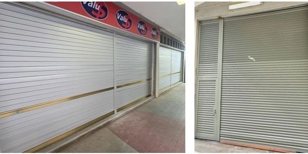 Closed metal roller shutters on storefronts in an indoor market.