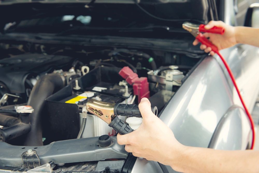 Hands holding jumper cable clamps near a car battery for jump-starting.