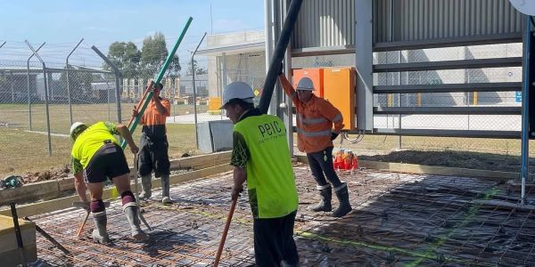 Workers preparing concrete foundation with tools at a construction site.