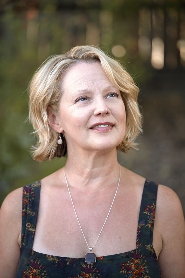 Blonde woman with a thoughtful expression in a floral dress and pendant necklace.