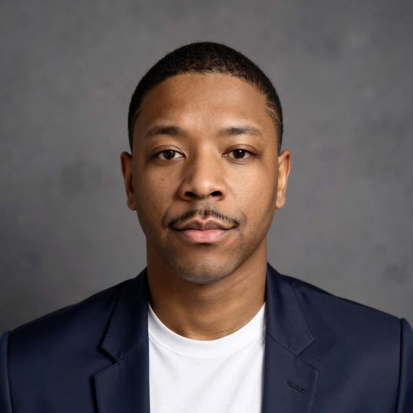 Man in navy blazer and white shirt posing against gray background.