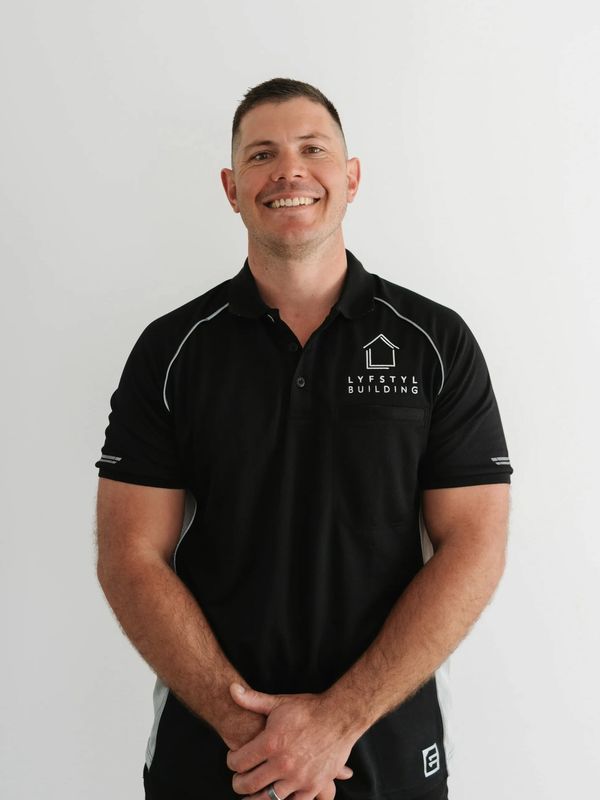 Smiling man in a black LYFSTYL BUILDING polo shirt stands against a plain white background.