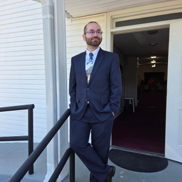 Man in a suit standing outside a building with hands in pockets.
