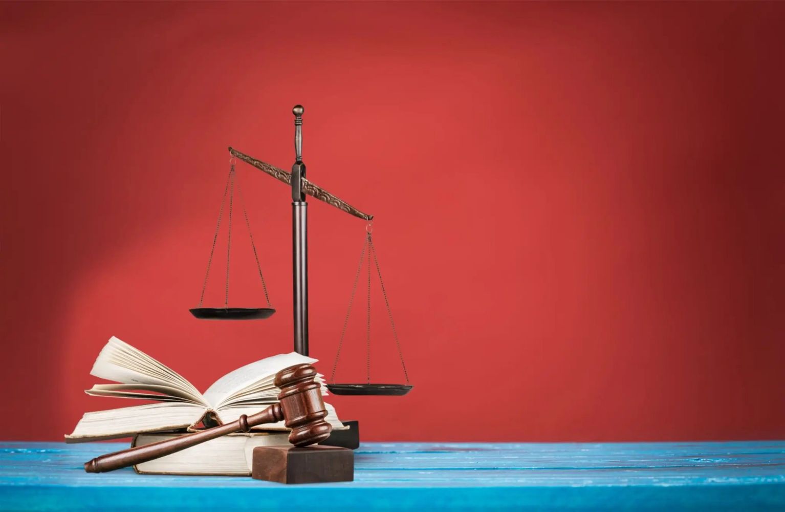 Gavel, scales of justice, and open law books on a blue table with red background.