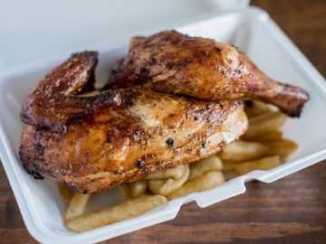 Grilled chicken leg quarters served with thick-cut fries in a takeout container.
