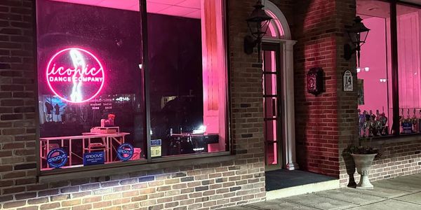 Night view of a dance studio with bright pink neon lights and trophies inside.