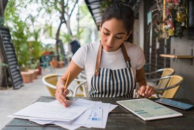 Woman business owner at a table with a tablet and phone reviewing reports.