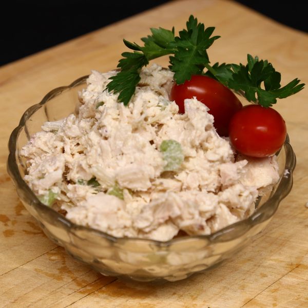 A bowl of chicken salad garnished with cherry tomatoes and parsley.