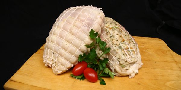 Two stuffed meat rolls on a wooden board with tomatoes and parsley.