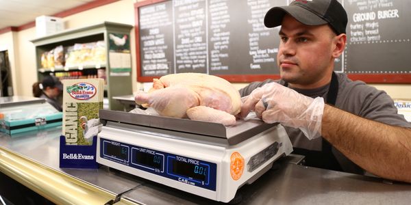 Man weighing whole chicken at a deli counter.