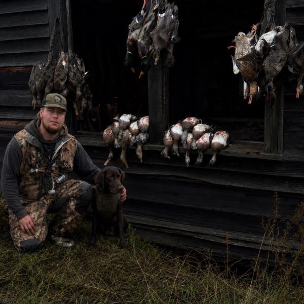 Hunter with his dog posing next to a collection of hunted ducks and birds.