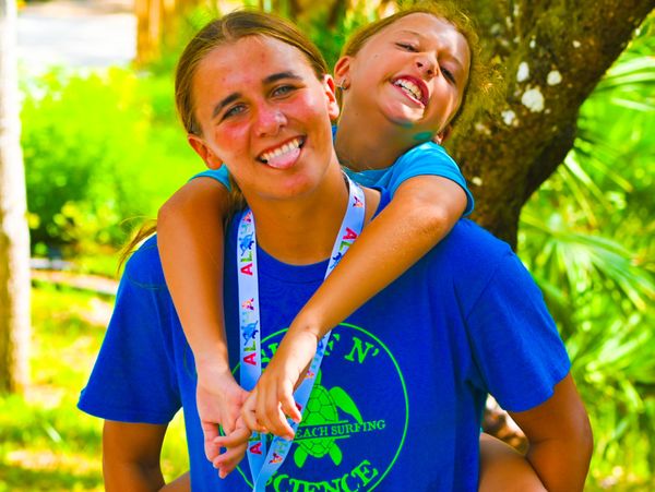 Two smiling children enjoying a playful piggyback in a sunny outdoor setting.