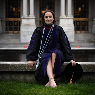 A female in graduate regalia sitting on a fountain