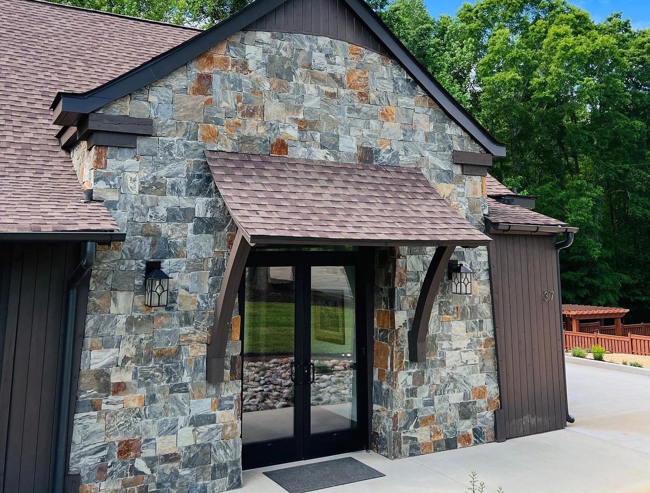 Stone house entrance with glass double doors and wooden awning.