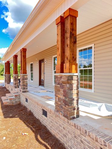 New porch with stone pillars and wooden beams under bright blue sky.