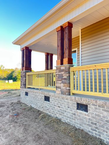 New porch with wooden railings, stone pillars, and brick foundation under a clear blue sky.