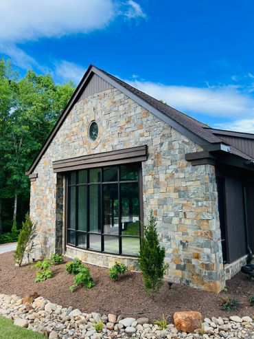 Stone house with large window and landscaped garden under a blue sky.