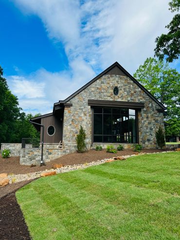 Stone house with large windows and green lawn under a partly cloudy blue sky.