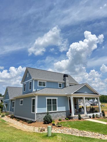 Blue two-story house with a front porch under a bright sky.