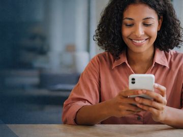 Smiling woman using smartphone at a table.