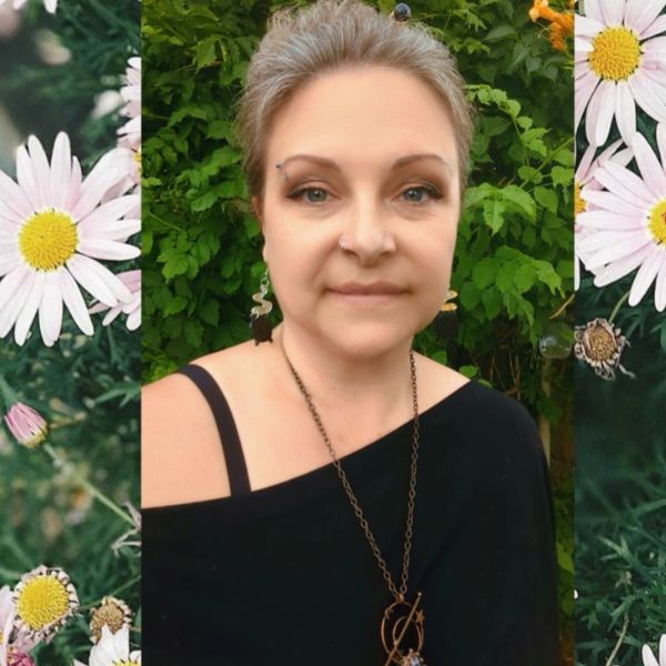 Woman with face makeup and jewelry in front of greenery.