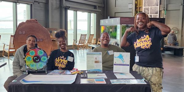 Four people smiling at an informational booth indoors.