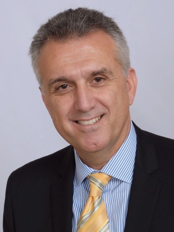 Middle-aged man smiling in a formal suit and yellow tie.