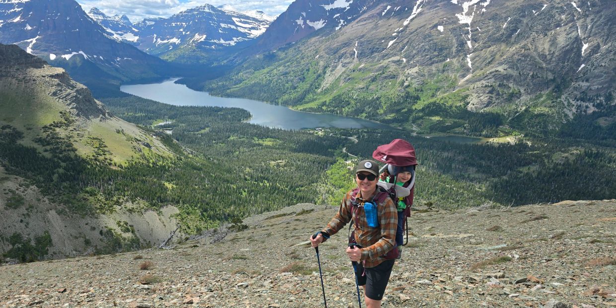 Hiker with child on a mountainous trail overlooking a lake.