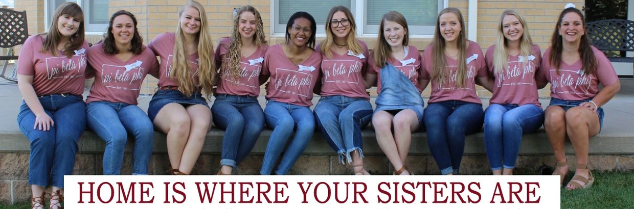 Sisters sitting together with a sign saying home is where your sisters are.