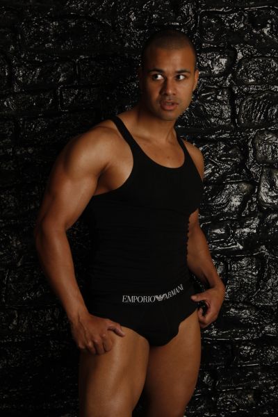 Muscular man posing against a black textured wall.