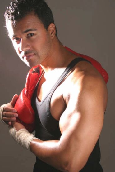 Muscular boxer holding red gloves and smiling.