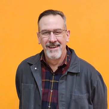 Smiling middle-aged man in glasses against an orange background.