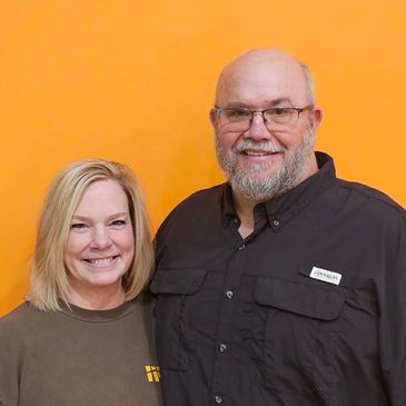Smiling middle-aged couple posing in front of an orange background.