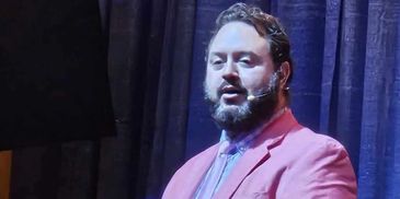 Man in a pink suit speaking at a podium with a microphone.