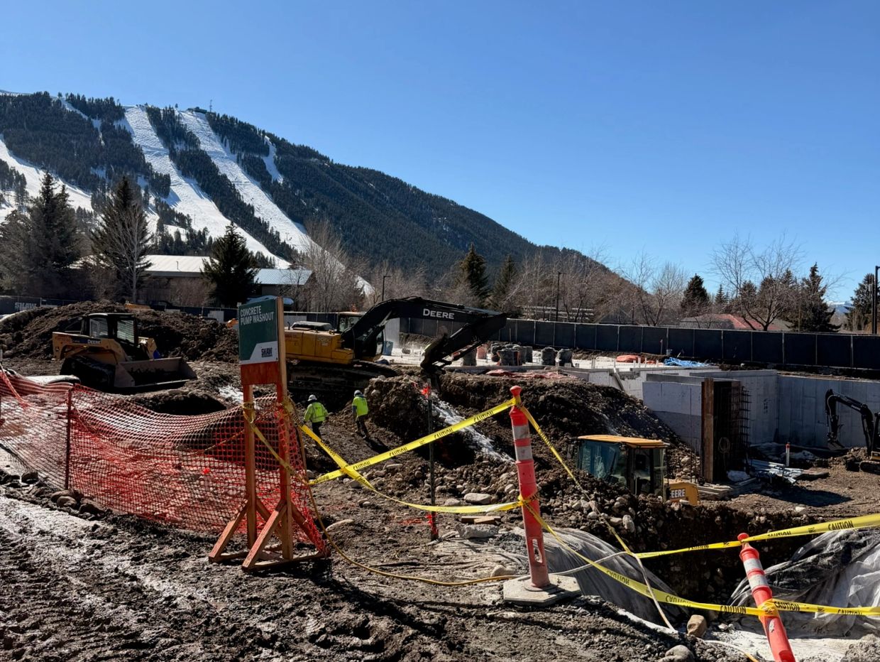 Construction site with equipment and workers near snowy mountain slopes.