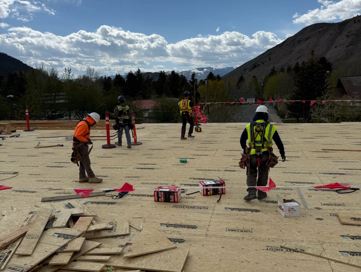Construction workers on a rooftop with safety gear and mountains in the background.