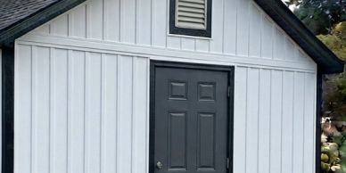 Small white shed with a black door.