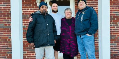 Group photo of four people outside a brick house.