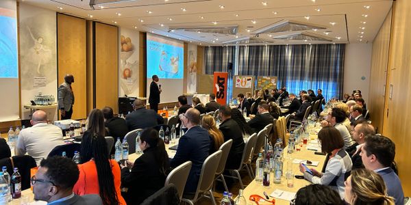 A professional conference with attendees listening to a presentation in a large room.