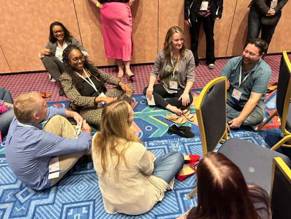 A group of people sitting on a colorful carpet, engaging in conversation.