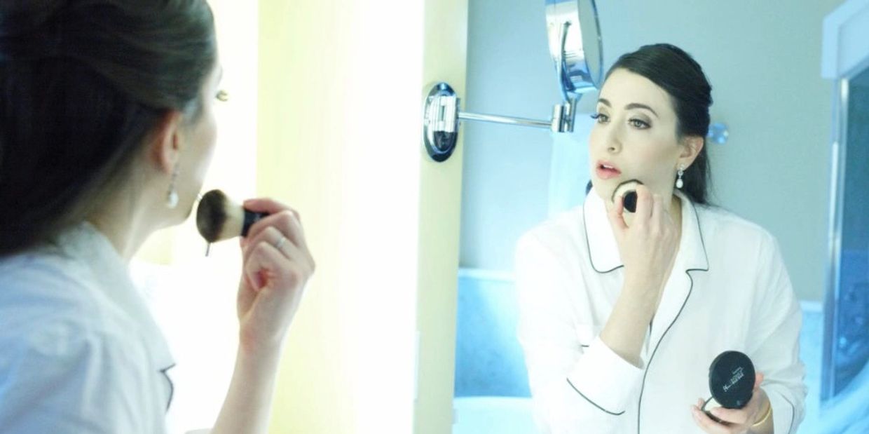 Bride admiring herself in the mirror while touching up her makeup, showcasing a flawless bridal look.
