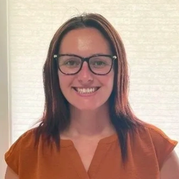 Smiling woman with glasses and brown hair wearing an orange top.