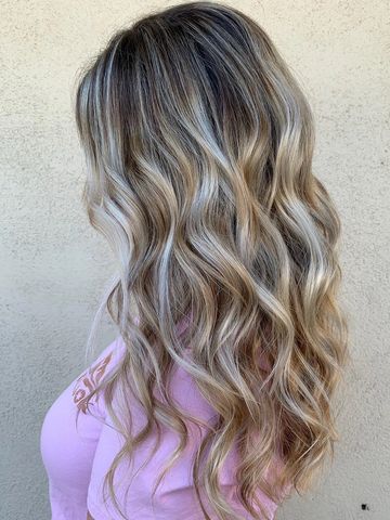 Long wavy blonde hair with dark roots against a neutral background.
