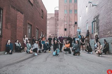 A diverse group posing in an urban alleyway between brick buildings.