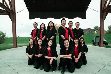 A group of twelve young people posing outdoors in coordinated black and red outfits.