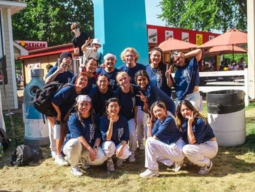 Group of young people in matching blue shirts posing outdoors with peace signs.